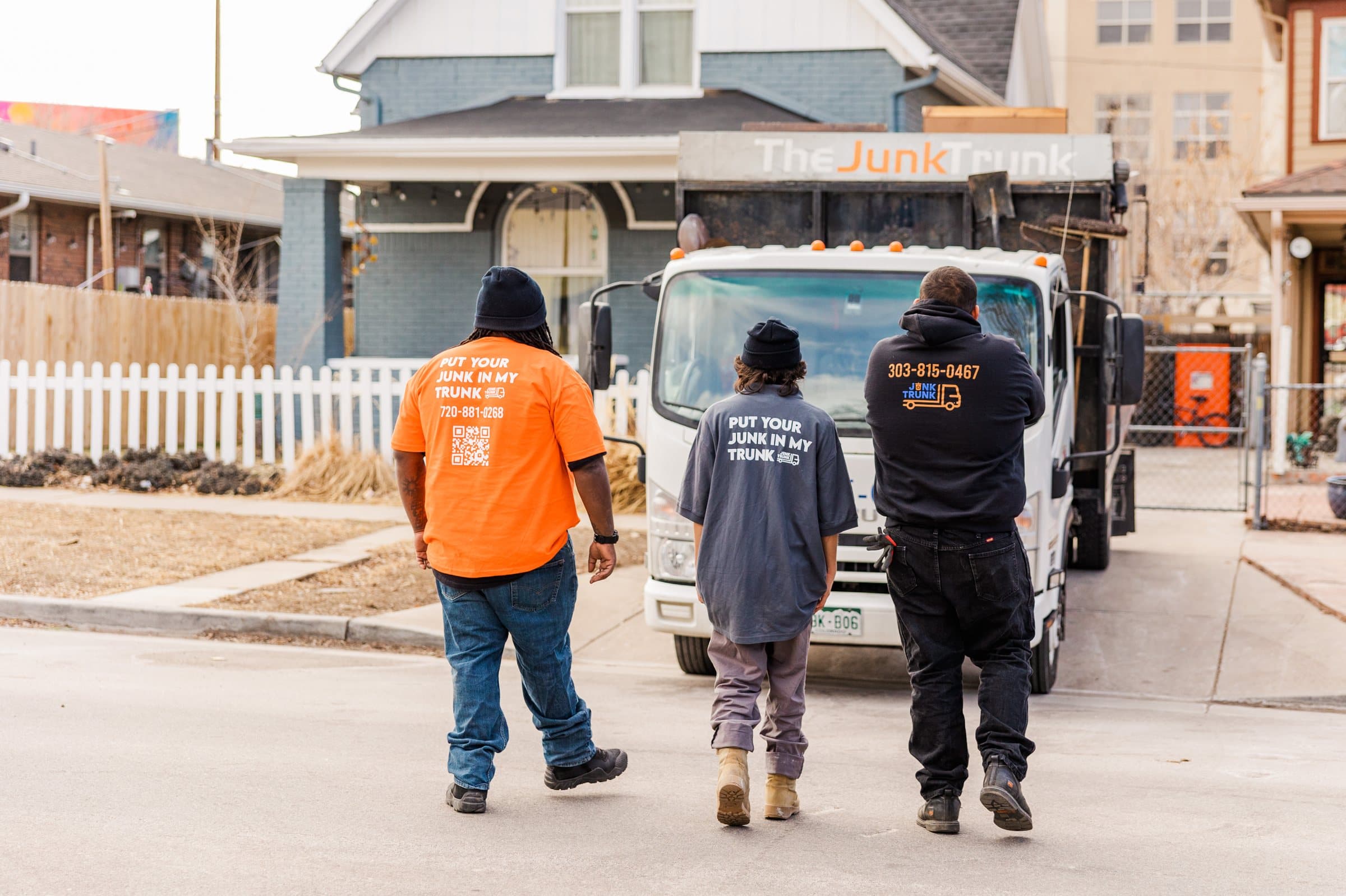 Junk Trunk crew walking toward a residential site with truck, fencing, and portable toilet setup