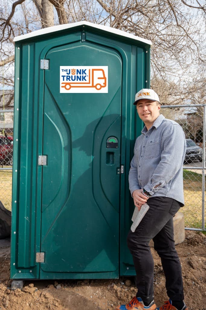 Nathan from The Junk Trunk next to a portable toilet on a job site